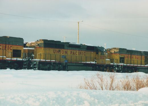 Three Union Pacific diesel locomotives, including #3027, are parked in a snow-covered yard under an overcast sky.