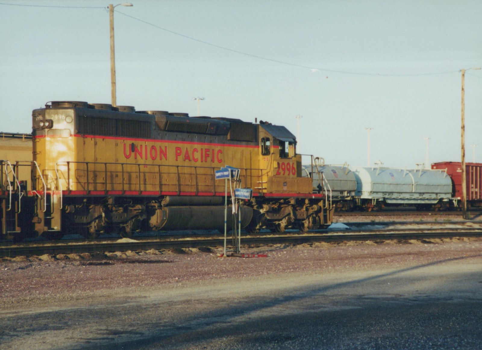 A side view of a yellow and black Union Pacific locomotive numbered 2996, stationary on a set of tracks with freight cars behind it, under a clear sky.
