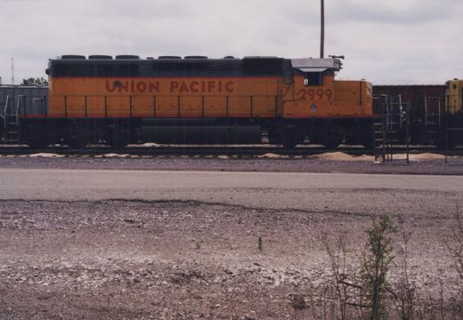 A side view of a Union Pacific diesel locomotive, number 2999, parked on tracks in a gravel yard under a cloudy sky.