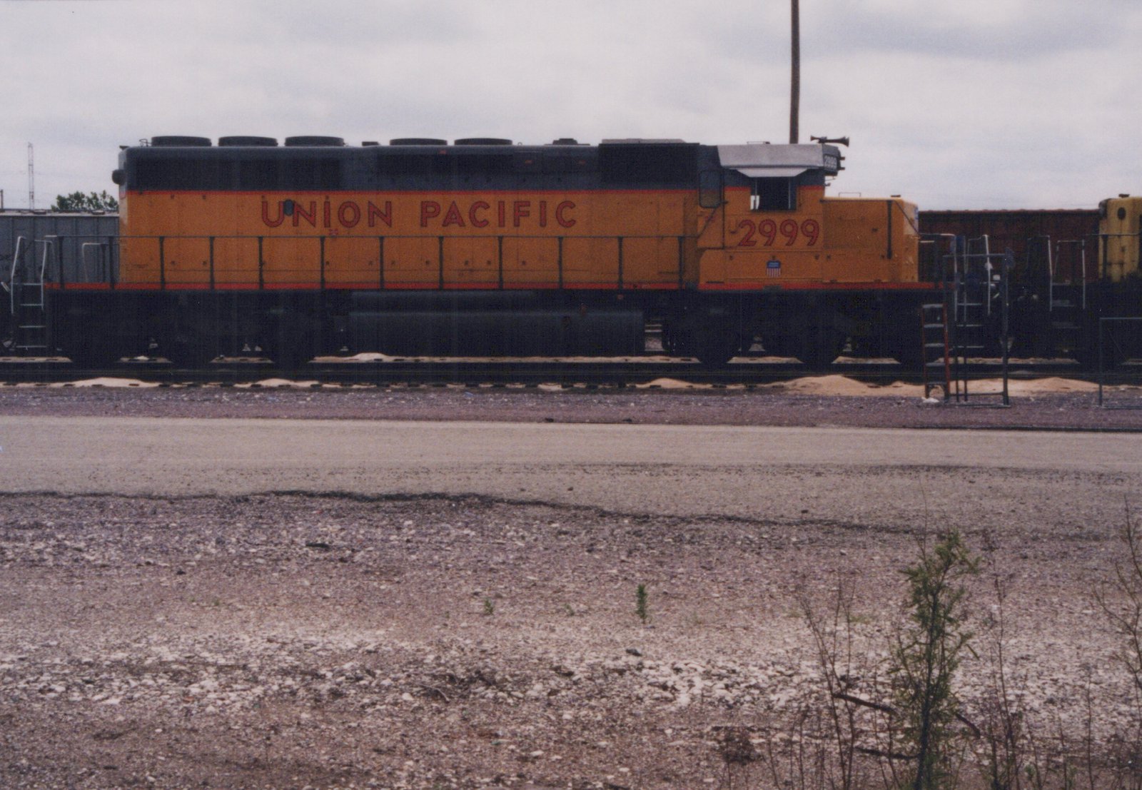 A side view of a Union Pacific diesel locomotive, number 2999, parked on tracks in a gravel yard under a cloudy sky.
