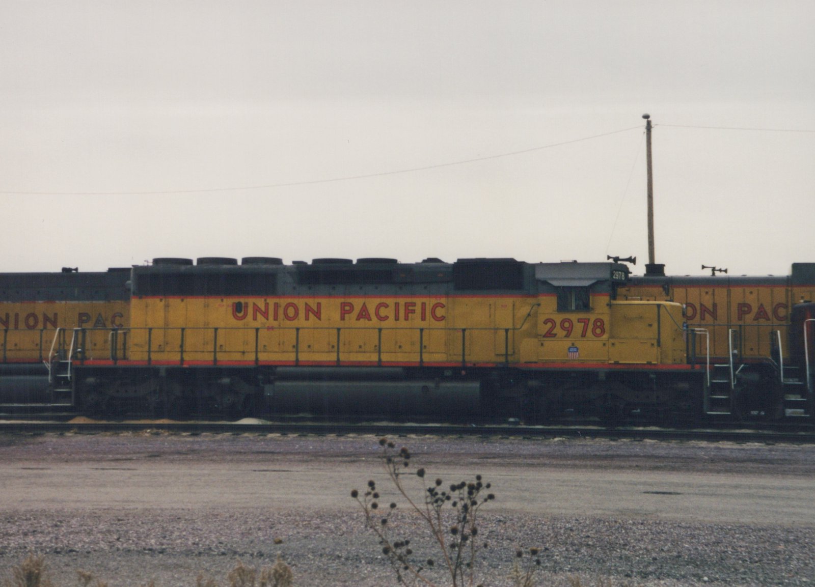 Side view of a yellow and gray Union Pacific diesel locomotive numbered 2978, parked on tracks in a gravel yard under a cloudy sky.