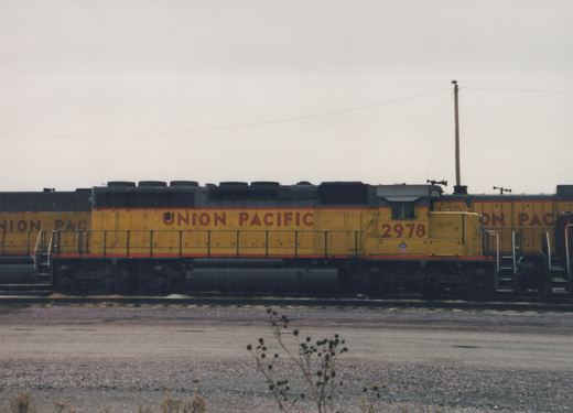 Side view of a yellow and gray Union Pacific diesel locomotive numbered 2978, parked on tracks in a gravel yard under a cloudy sky.