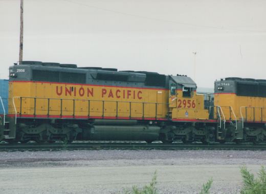Side view of two yellow and gray Union Pacific diesel locomotives, numbers 2956 and 5946, parked on parallel tracks in a gravel yard under a cloudy sky.