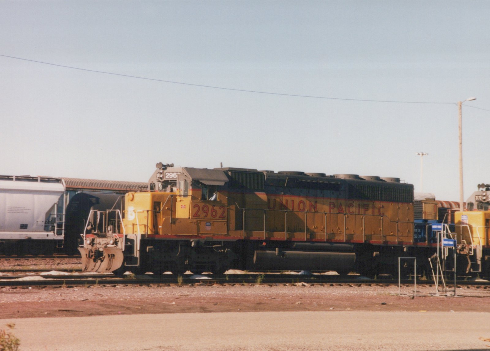 Yellow Union Pacific diesel locomotive number 2962 sits on the tracks in a rail yard with another locomotive and freight cars nearby.