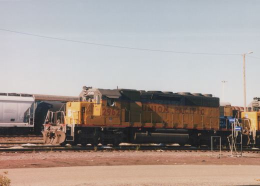 Yellow Union Pacific diesel locomotive number 2962 sits on the tracks in a rail yard with another locomotive and freight cars nearby.