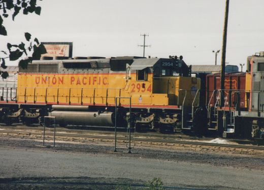 Side view of a yellow Union Pacific diesel locomotive numbered 2954 in a rail yard, with a maroon Wisconsin Central boxcar visible behind it.