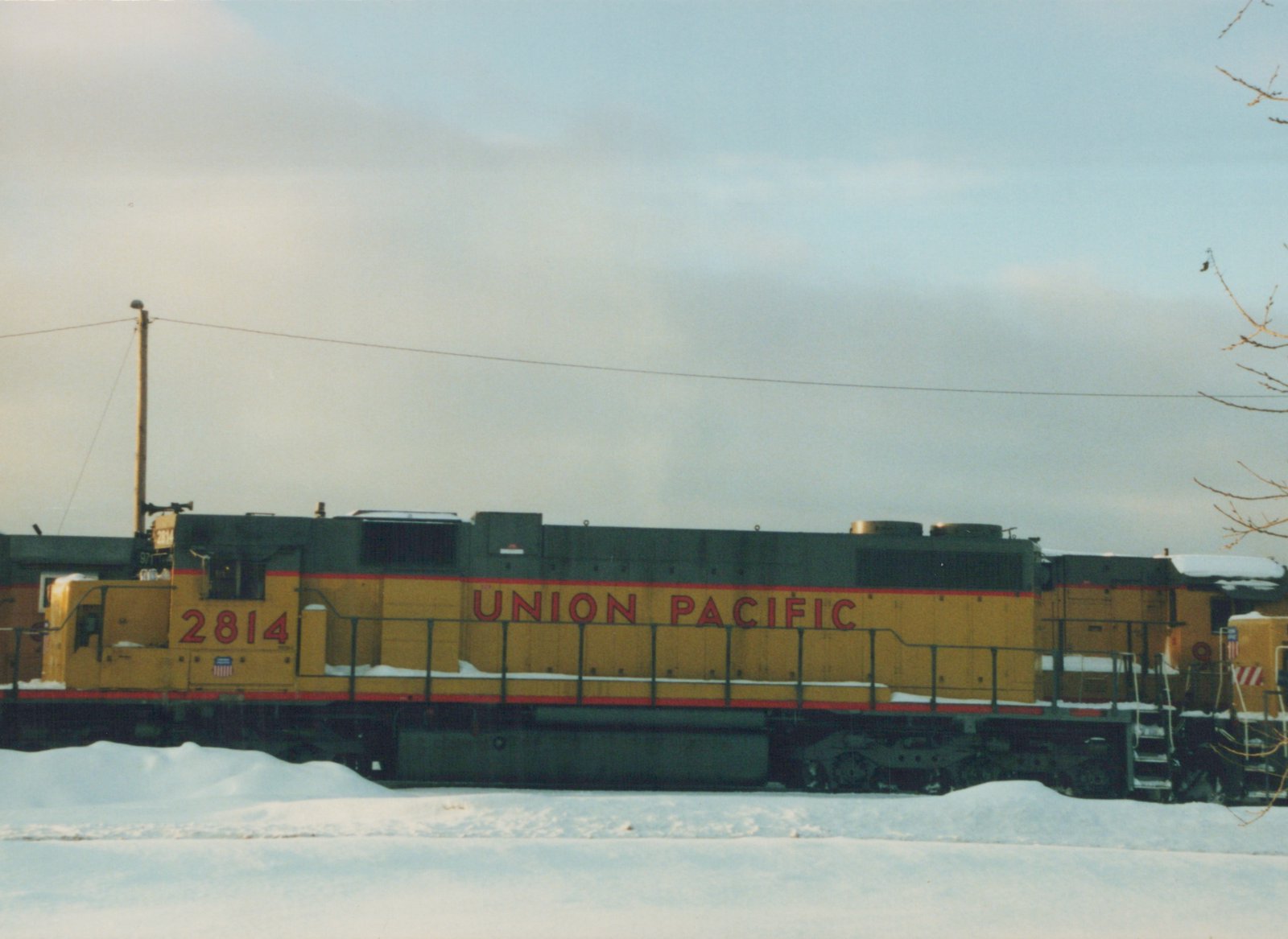 A side view of a yellow and black Union Pacific diesel locomotive numbered 2814, sitting on tracks in a snow-covered yard under an overcast sky.