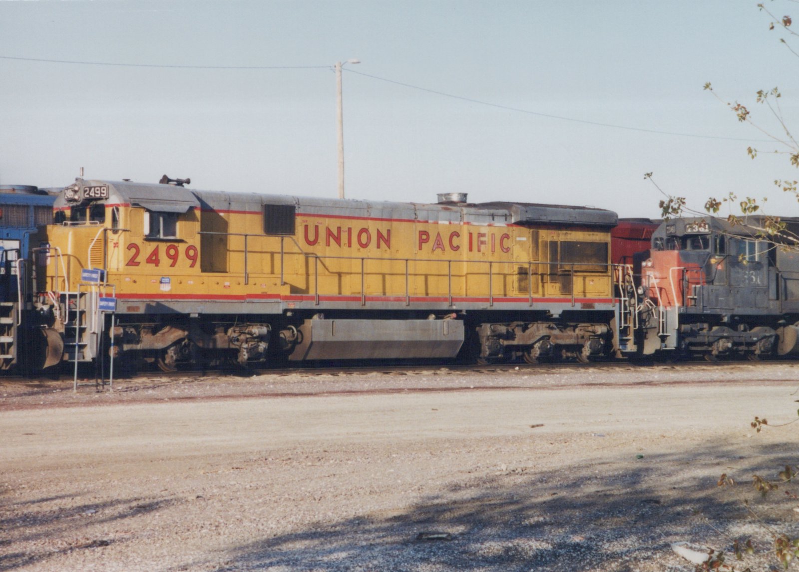 A yellow Union Pacific diesel locomotive numbered 2499 sits on tracks in a rail yard, with a gray locomotive numbered 7361 visible behind it.