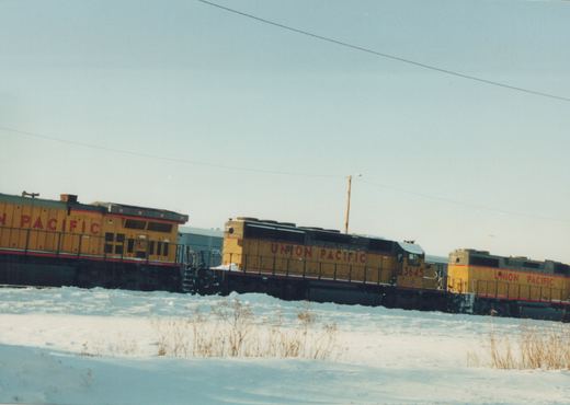 Side view of two yellow Union Pacific diesel locomotives, one marked 3645, on a snowy railroad track, with a Canadian National freight car behind them.