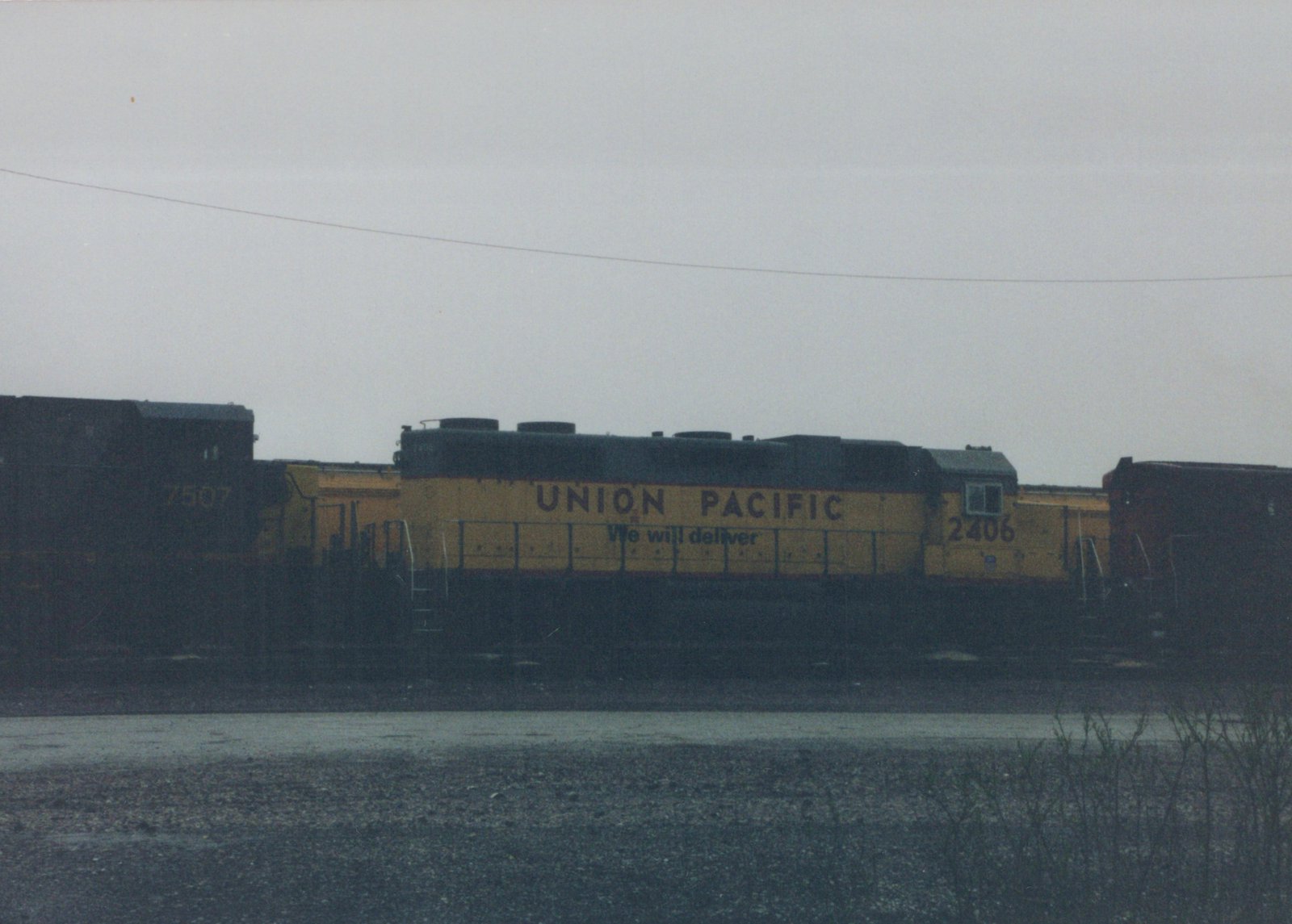 Side view of a yellow and gray Union Pacific diesel locomotive, number 2406, parked on tracks in a yard with another locomotive visible behind it.