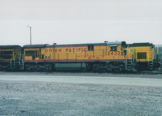 A side view of two yellow Union Pacific diesel locomotives in a gravel yard on an overcast day, with the lead locomotive numbered 2433.