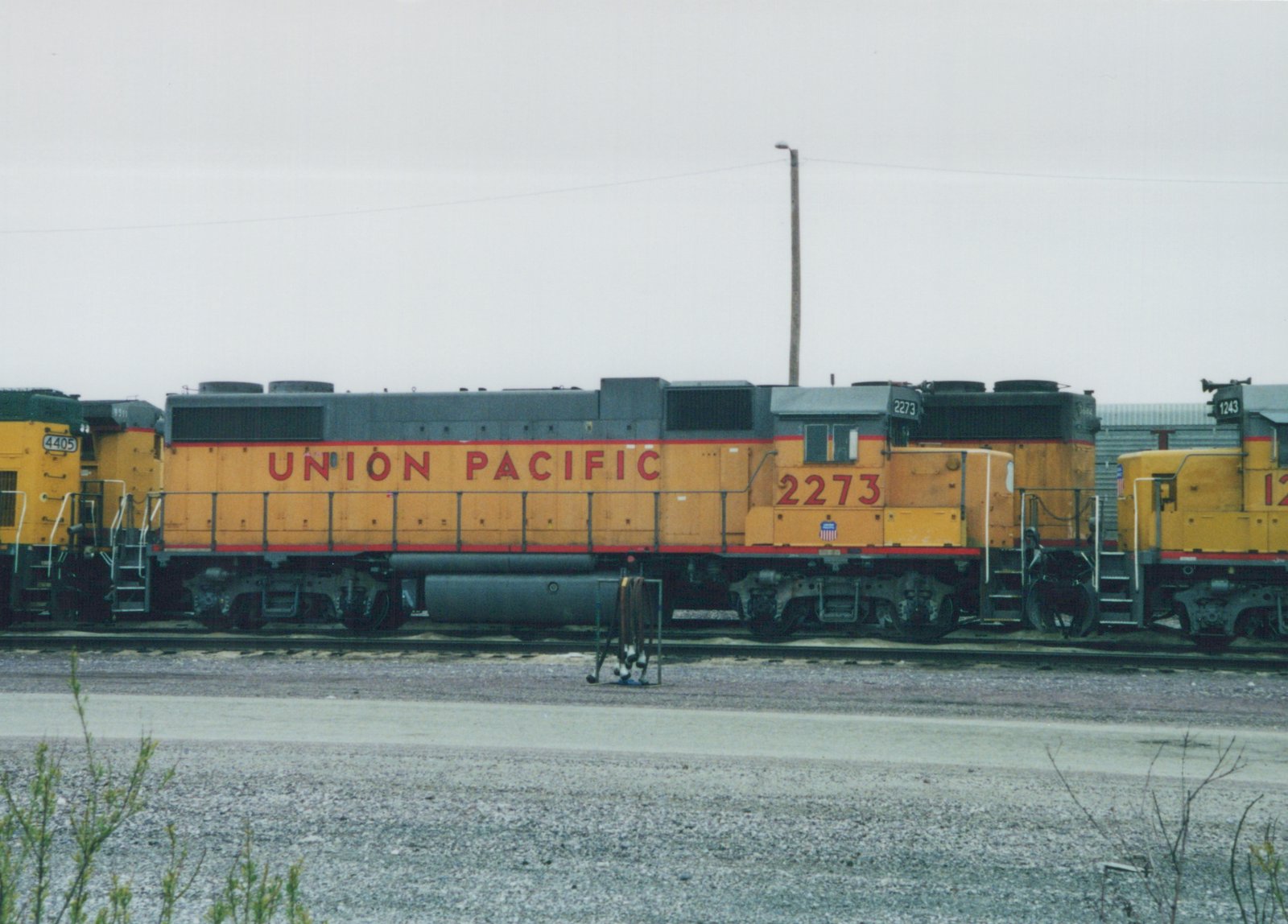Side view of a yellow Union Pacific diesel locomotive, number 2273, in a gravel yard with other locomotives visible.