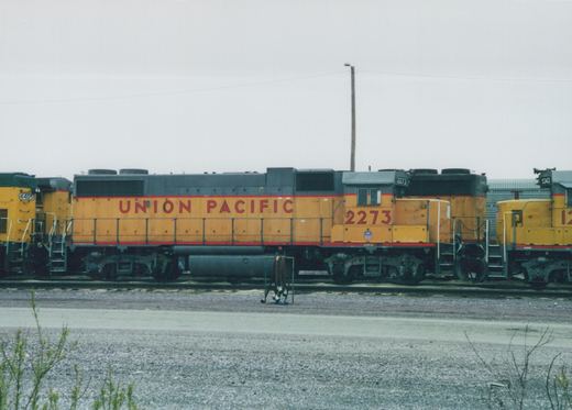 Side view of a yellow Union Pacific diesel locomotive, number 2273, in a gravel yard with other locomotives visible.