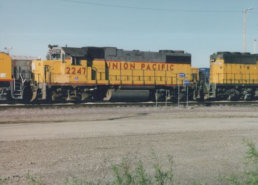 Two yellow and gray Union Pacific diesel locomotives, numbered 2247 and 6847, sit on parallel tracks in a gravel yard on a sunny day.
