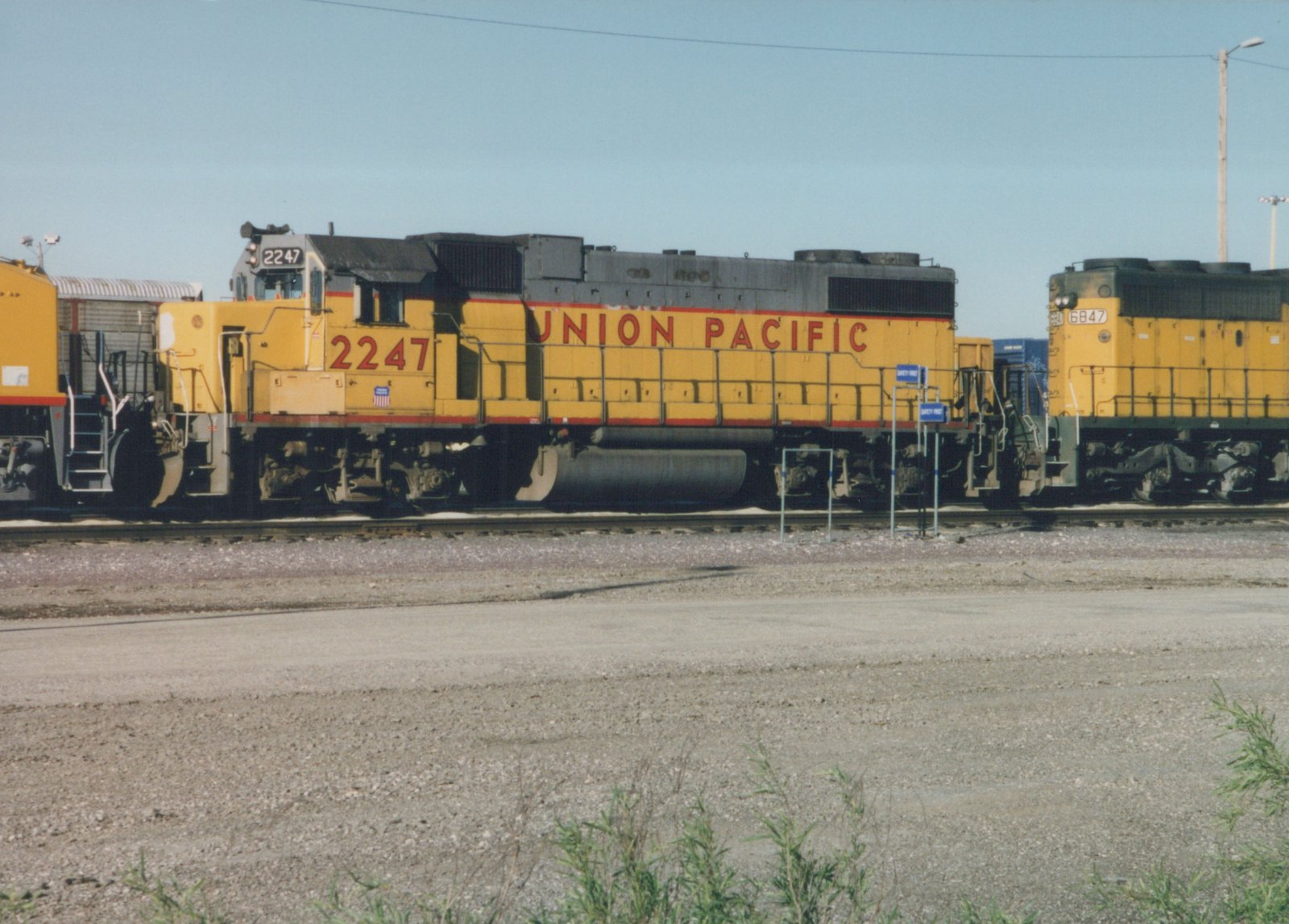 Two yellow and gray Union Pacific diesel locomotives, numbered 2247 and 6847, sit on parallel tracks in a gravel yard on a sunny day.