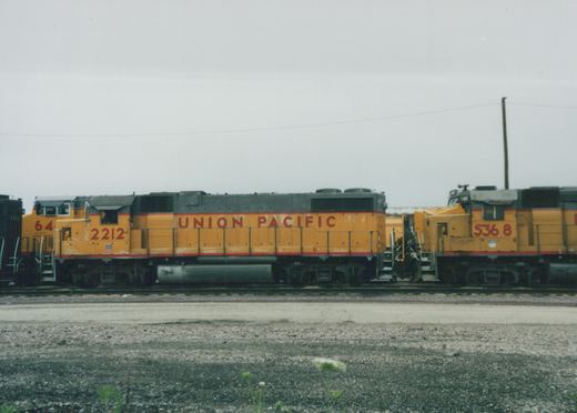 Side view of two yellow and gray Union Pacific diesel locomotives, numbered 2212 and 5368, parked on adjacent tracks in a gravel yard.