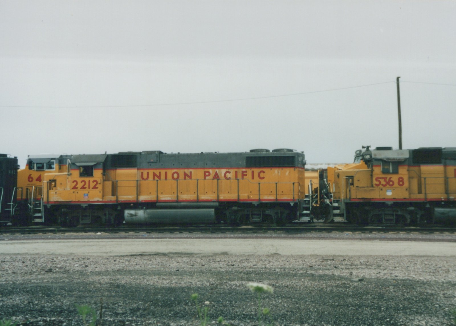 Side view of two yellow and gray Union Pacific diesel locomotives, numbered 2212 and 5368, parked on adjacent tracks in a gravel yard.