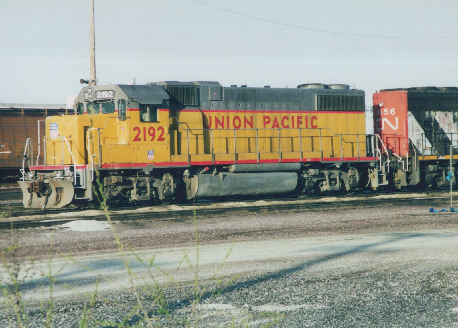 A yellow and red Union Pacific locomotive numbered 2192 is parked on tracks in a rail yard, with a second locomotive behind it.