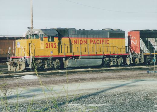 A yellow and red Union Pacific locomotive numbered 2192 is parked on tracks in a rail yard, with a second locomotive behind it.