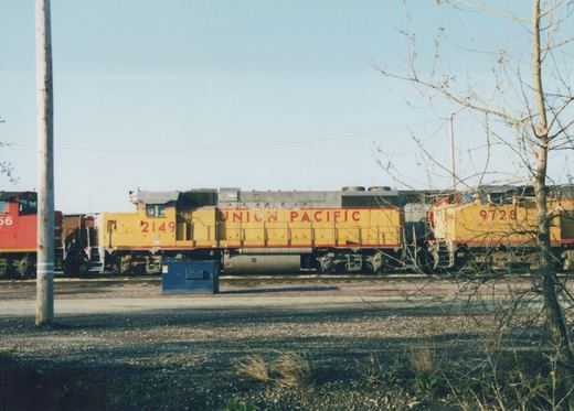 Two yellow and red Union Pacific locomotives, numbers 2149 and 9728, stand coupled on tracks in a yard, with a leafless tree and a gravel foreground.