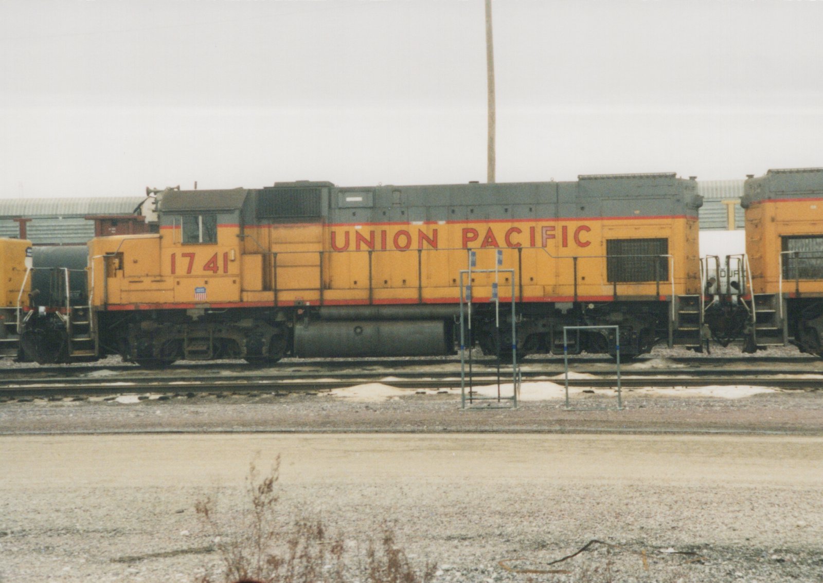 A yellow and gray Union Pacific locomotive numbered 1741 stands on tracks in a rail yard with snow on the ground.