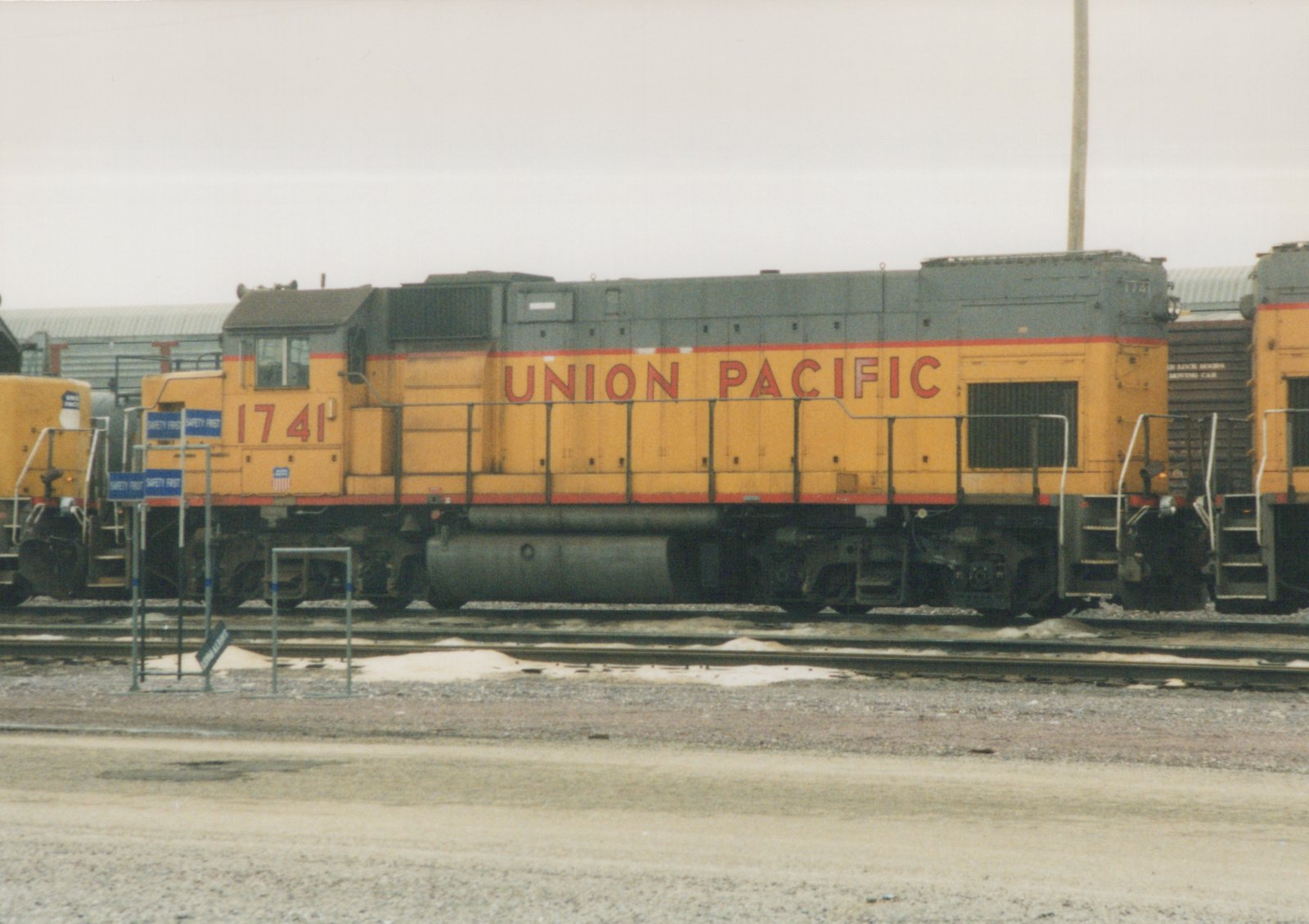 A yellow and gray Union Pacific locomotive with the number 1741 on its side is parked on tracks in a yard with patches of snow on the ground.