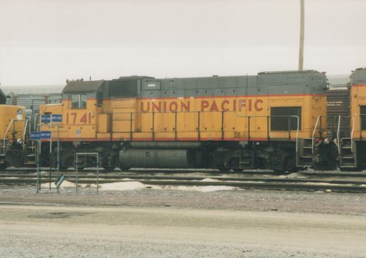 A yellow and gray Union Pacific locomotive with the number 1741 on its side is parked on tracks in a yard with patches of snow on the ground.