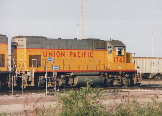 A yellow and gray Union Pacific diesel locomotive numbered 1740 sits on tracks next to a white boxcar in a rail yard.