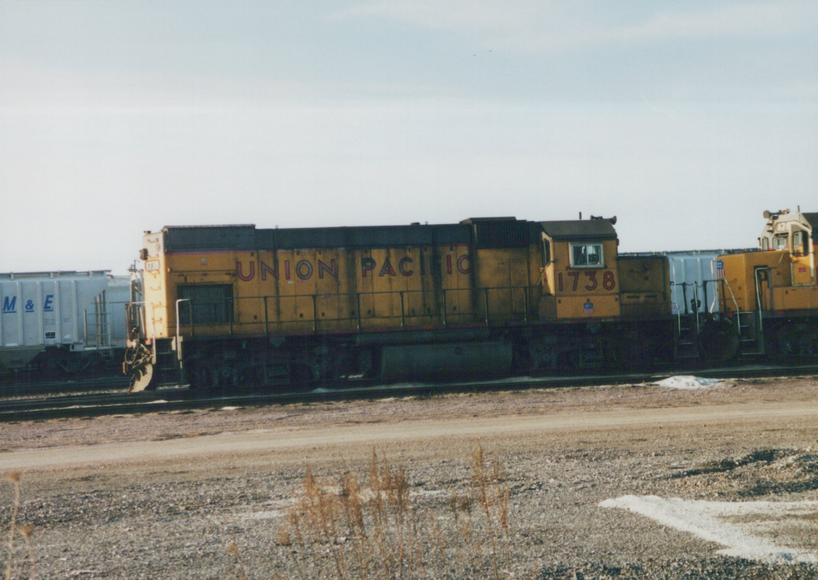 A yellow Union Pacific diesel locomotive numbered 1738 sits on tracks in a yard with snow patches on the ground, with a white freight car visible behind it.
