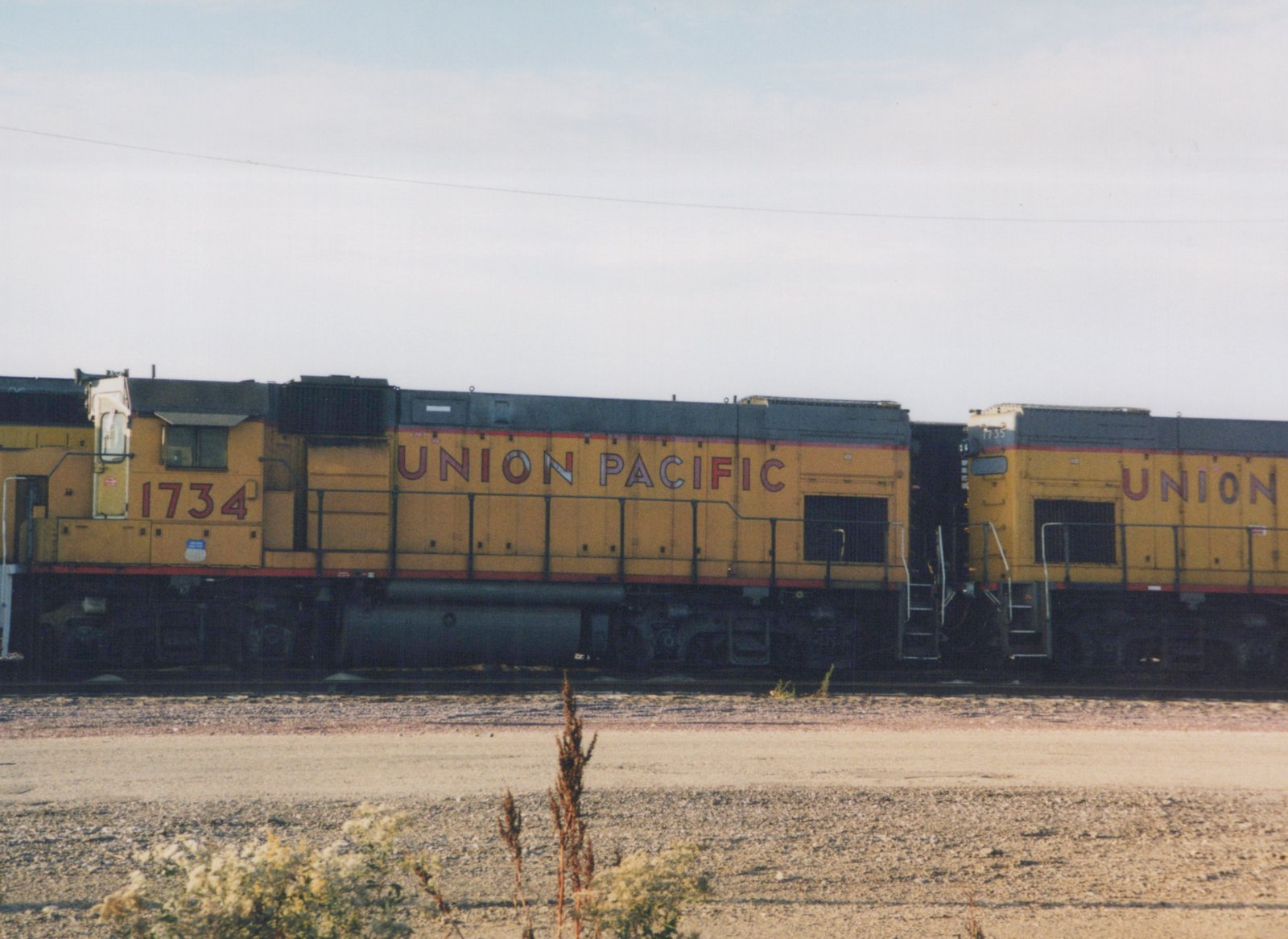 Two yellow Union Pacific diesel locomotives numbered 1734 and 1735 sit side by side on tracks in a gravel yard under a clear sky.