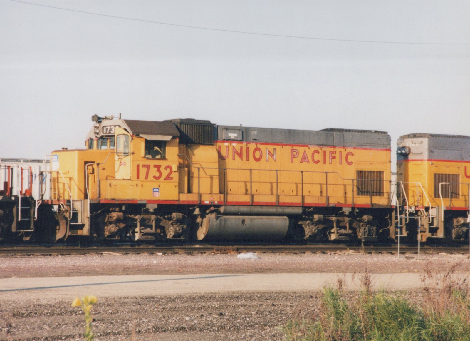 A side view of two yellow Union Pacific diesel locomotives with red stripes, numbered 1732 and 1740, standing on tracks in a gravel yard under a clear sky.