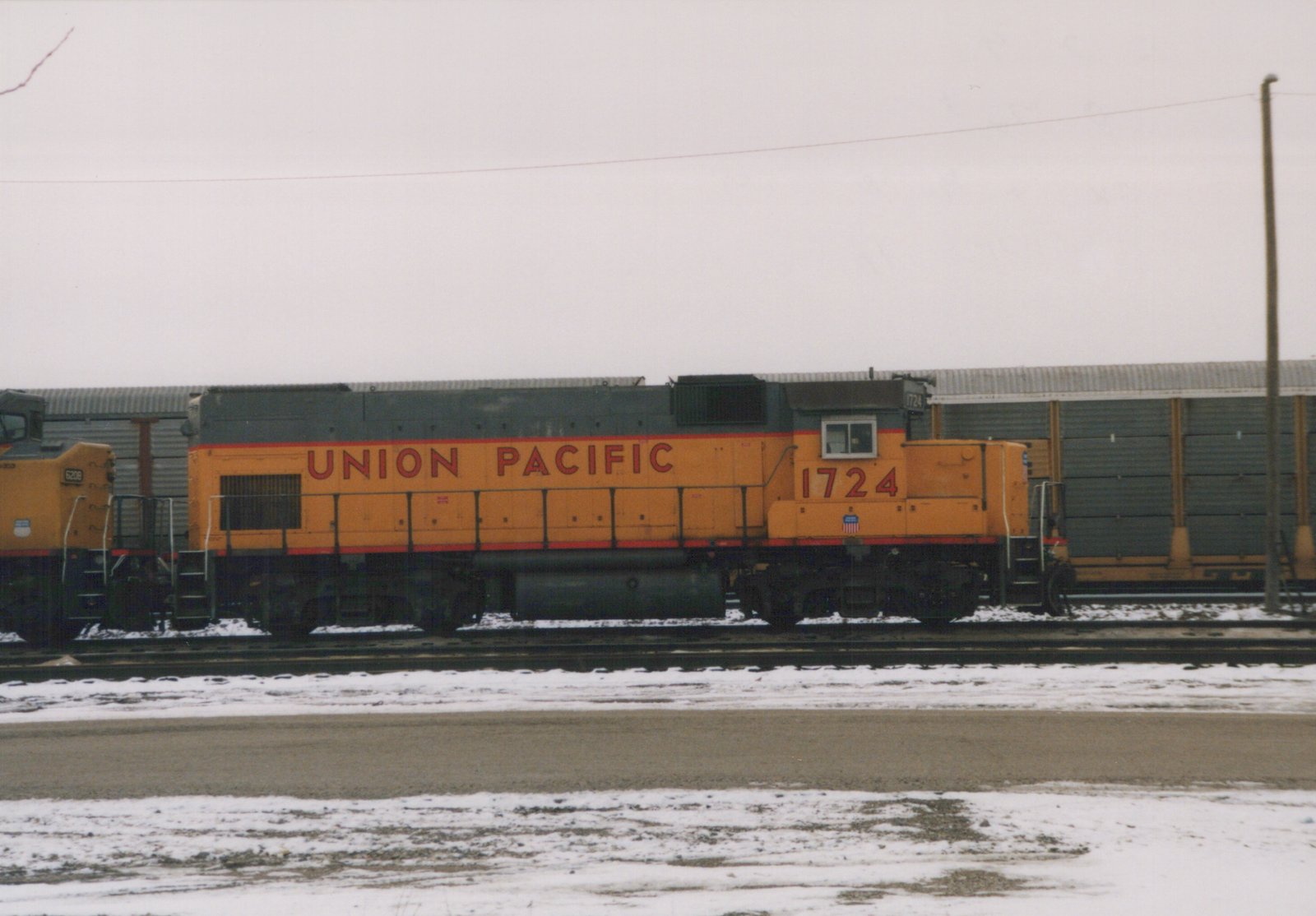 A yellow and grey Union Pacific diesel locomotive numbered 1724 stands on tracks in a snow-covered yard, with another locomotive partially visible behind it.