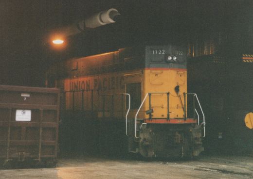 A yellow and black Union Pacific locomotive, number 1722, stands in a dark rail yard next to a brown freight car marked with the number 7.