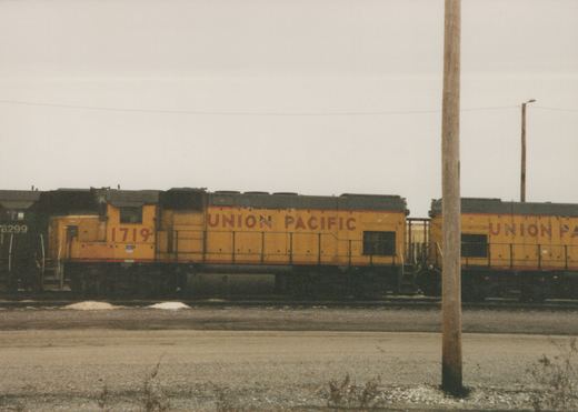 A yellow Union Pacific diesel locomotive, number 1719, is parked on a railroad track in a yard on a winter day.