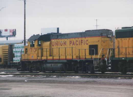 A side view of a yellow Union Pacific diesel locomotive, number 1713, parked on tracks in a rail yard with snow on the ground.