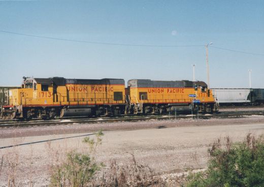 Two yellow and gray Union Pacific diesel locomotives, numbered 1713 and 1717, stand side-by-side on railroad tracks in an open yard under a clear sky with some dry vegetation in the foreground.