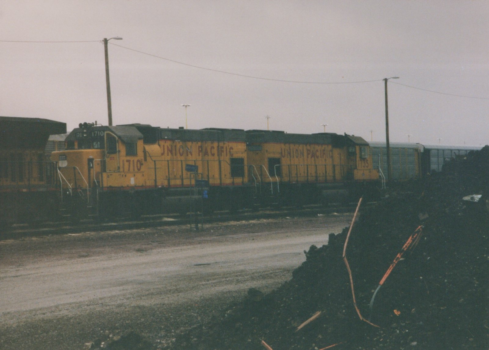 A side view of two yellow Union Pacific diesel locomotives, numbered 1710 and 1735, standing on tracks in a yard under a gray sky.