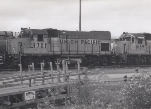 Black and white photo of two Union Pacific diesel locomotives, numbers 1701 and 1689, standing on parallel tracks in a yard with some wooden equipment in the foreground.