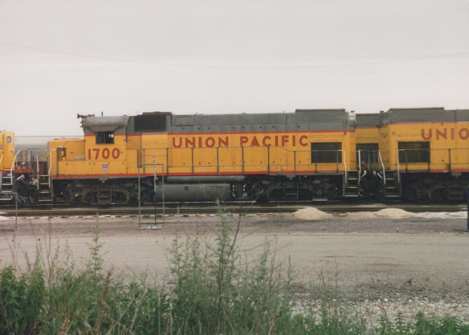 Side view of two yellow Union Pacific diesel locomotives, numbered 1700 and 705, parked on tracks in a gravel yard under an overcast sky.