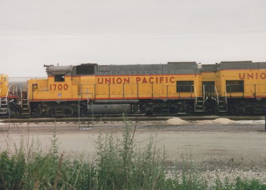Side view of two yellow Union Pacific diesel locomotives, numbered 1700 and 705, parked on tracks in a gravel yard under an overcast sky.