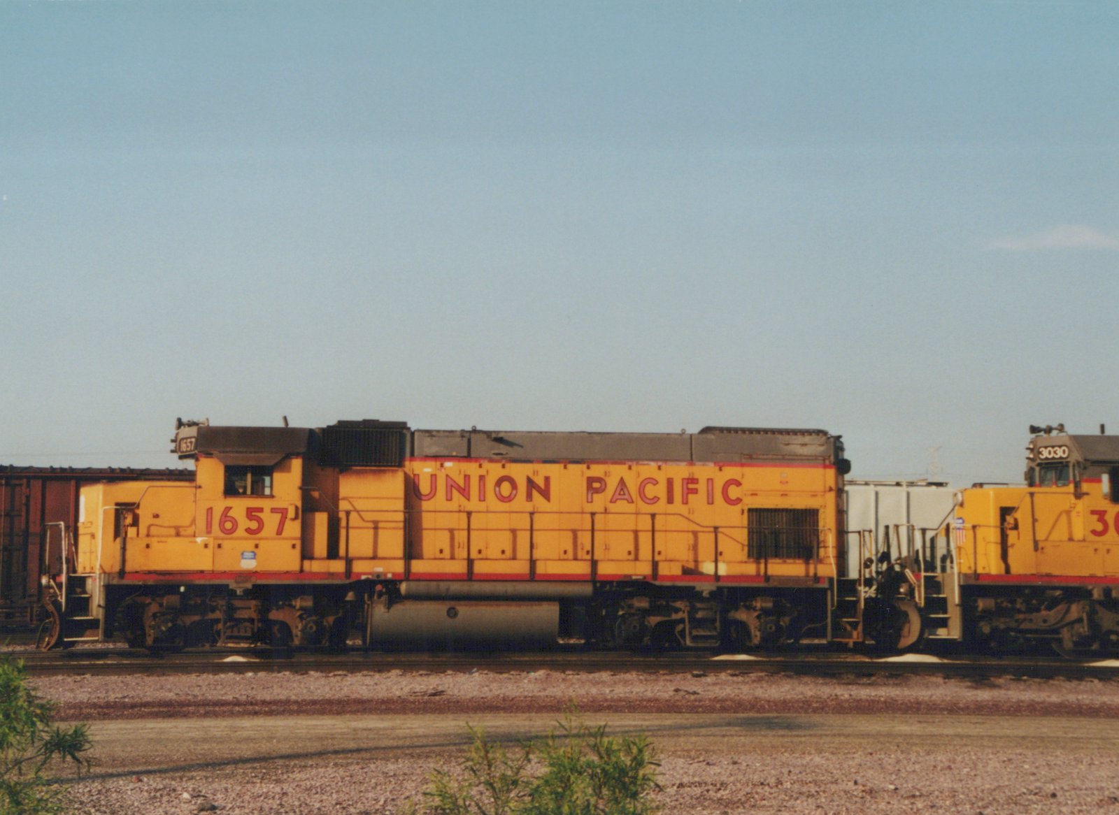 Side view of two yellow Union Pacific diesel locomotives, including #1657, standing on tracks in a gravel yard with a clear blue sky above.
