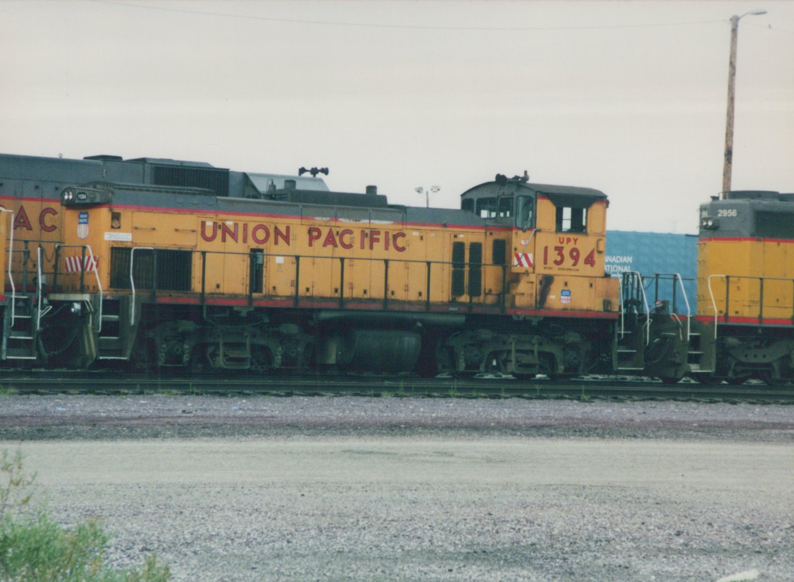 Side view of two Union Pacific diesel locomotives, numbered 1394 and 2956, in a gravel rail yard on an overcast day.