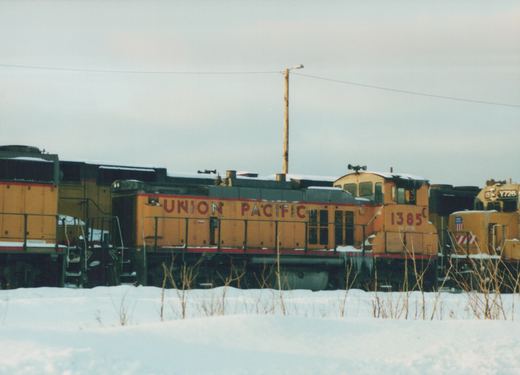Two yellow and red Union Pacific diesel locomotives, numbers 1385 and Y726, are parked side by side in a snowy yard under an overcast sky.