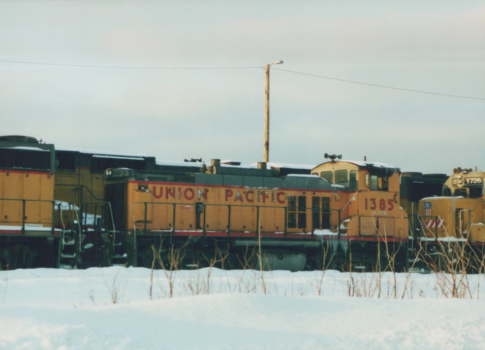 Two yellow and red Union Pacific diesel locomotives, numbers 1385 and Y726, are parked side by side in a snowy yard under an overcast sky.