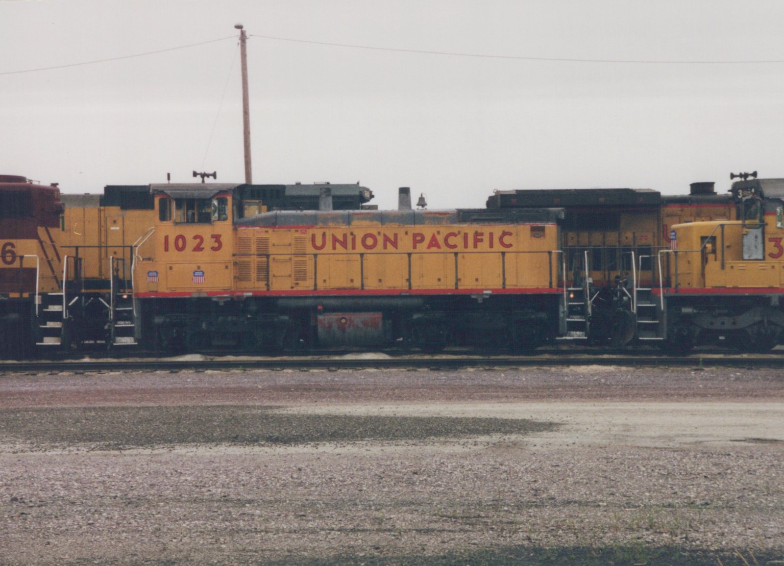 Side view of three Union Pacific diesel locomotives, with number 1023 in the center, parked on tracks in a gravel yard under a gray sky.