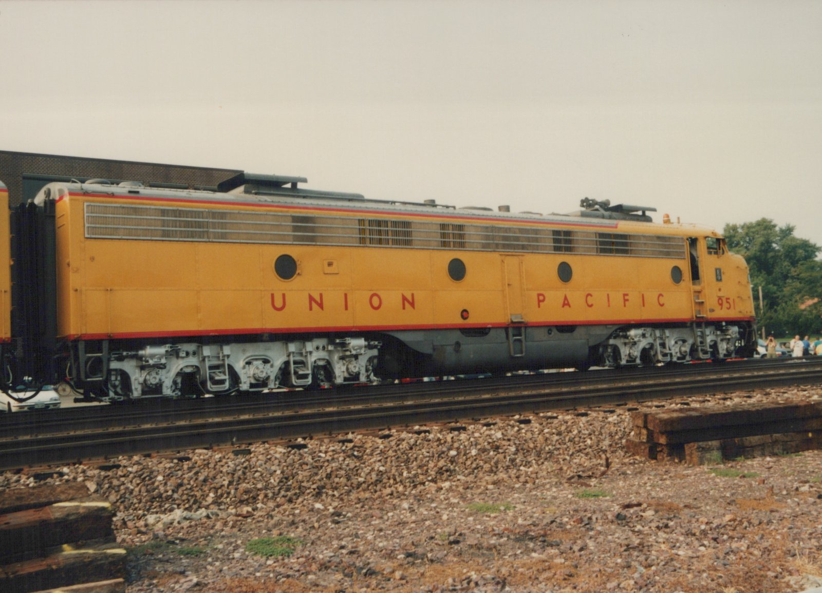 A side view of a yellow Union Pacific E9 diesel locomotive numbered 951, sitting on railroad tracks with people and trees in the background.