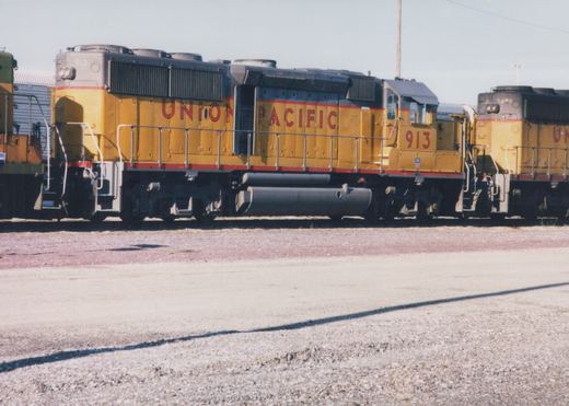 A side view of a yellow Union Pacific locomotive, number 913, standing in a gravel yard next to a second similar locomotive under a clear sky.
