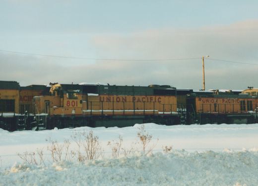 Two yellow and gray Union Pacific diesel locomotives, one numbered 801, are parked on a railroad track surrounded by snow under an overcast sky.