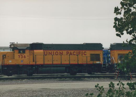 Side view of a yellow and black Union Pacific locomotive with the number 736, parked on tracks in a yard with another locomotive behind it.