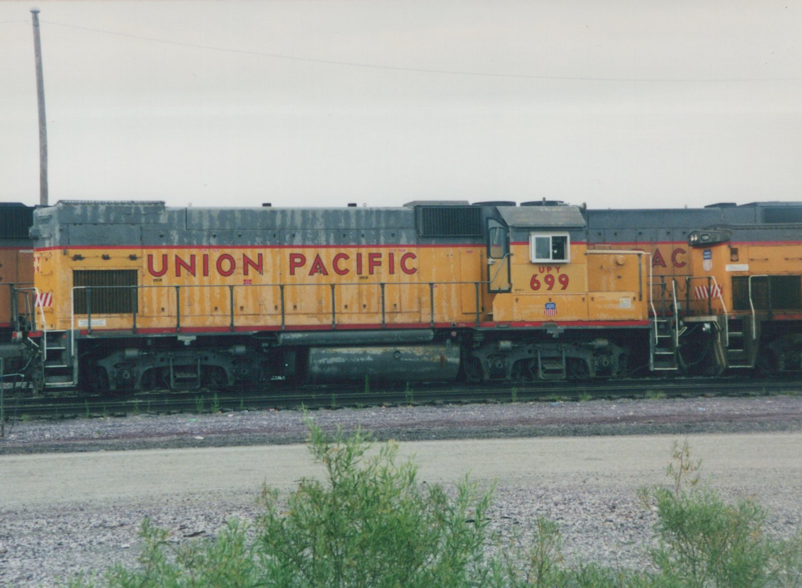 A side view of a yellow and red Union Pacific diesel locomotive numbered 699, parked in a gravel yard under an overcast sky.